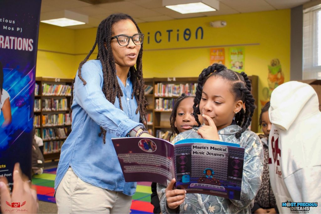Most Precious Dreams Foundation founder Mahogany Henderson engaging with a young reader holding Maria's Magical Music Journey during a children's literacy activity.